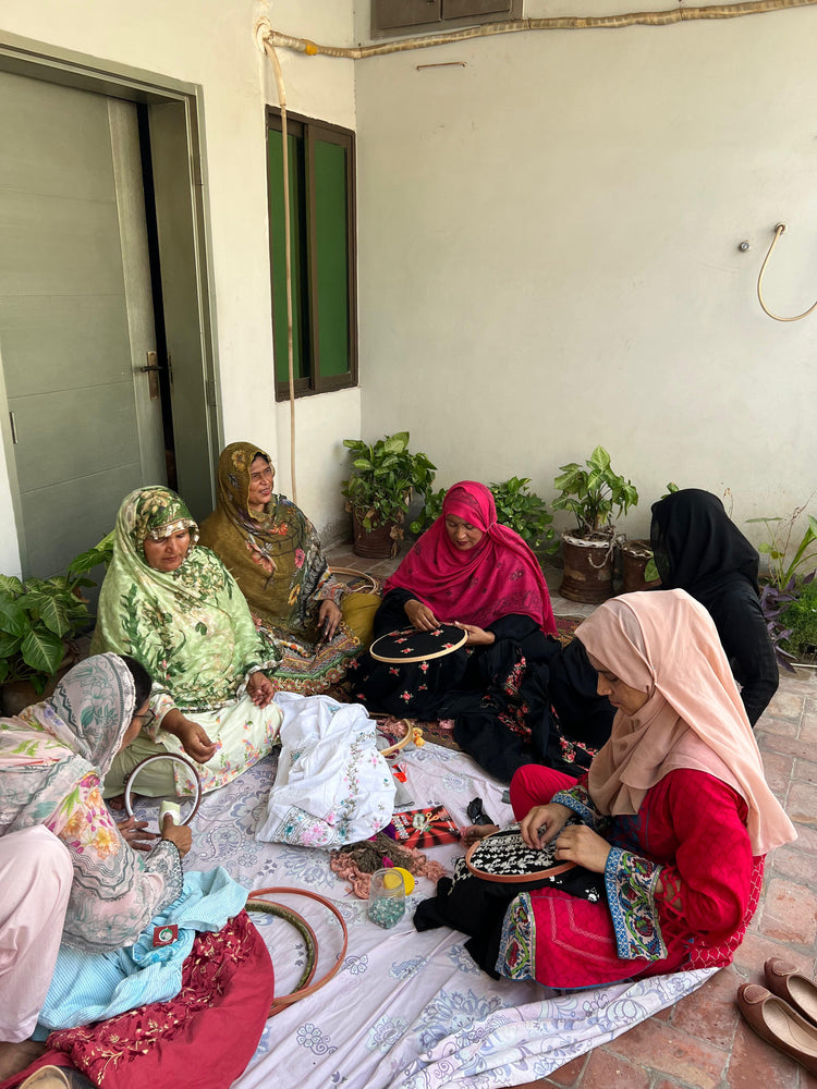 Women artisans sitting together, embroidering fabric by hand on wooden hoops